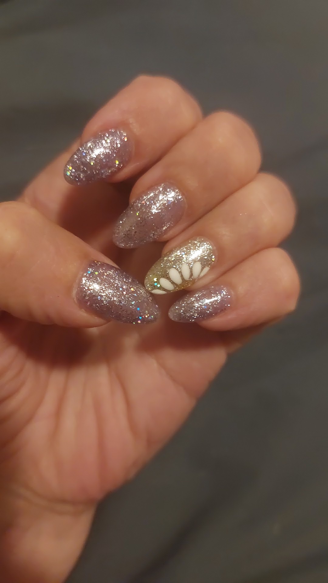 Amandelvormige glitternagels met een wit bloemetje op de ringvinger