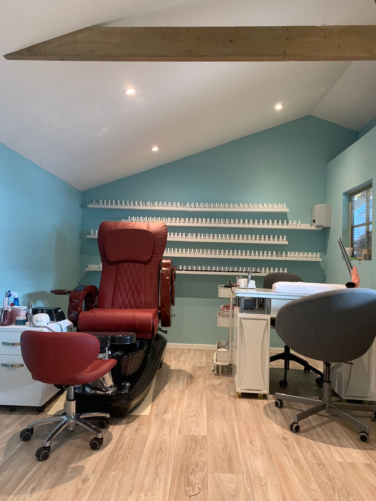 De salon van My My Nails in Druten: een rode pedicurestoel, witte planken vol nagellak tegen een aquablauwe muur en een werktafel